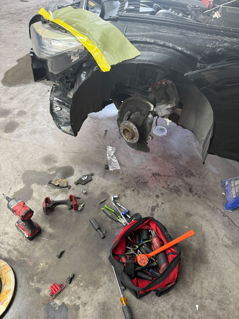 Front wheel hub with the brake rotor removed, old brake pads and caliper bracket on the garage floor