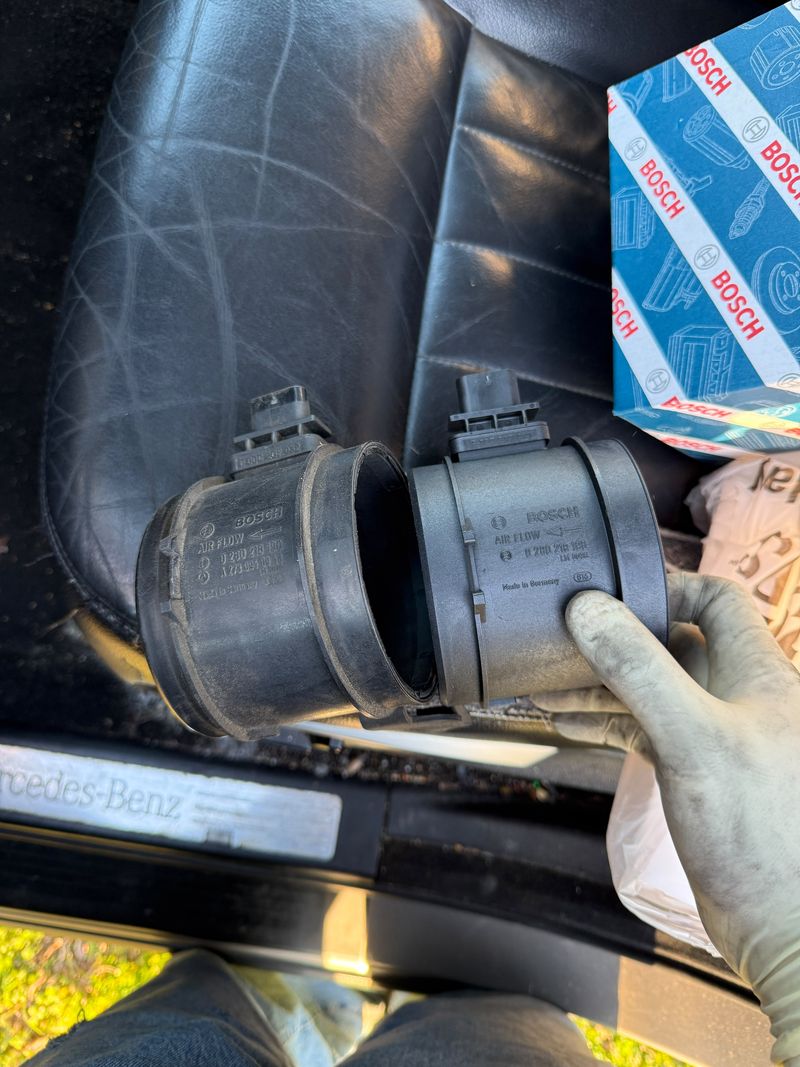 Old and new Bosch mass airflow sensors held next to a Mercedes-Benz door sill