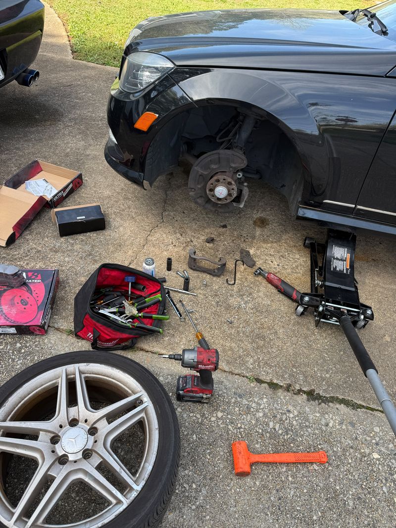 Mercedes-Benz with the front wheel off, new brake rotors and pads in their boxes on the driveway