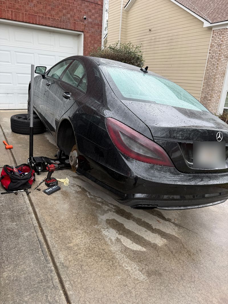 Black Mercedes-Benz on a floor jack with the rear wheel off and a new coated brake rotor fitted