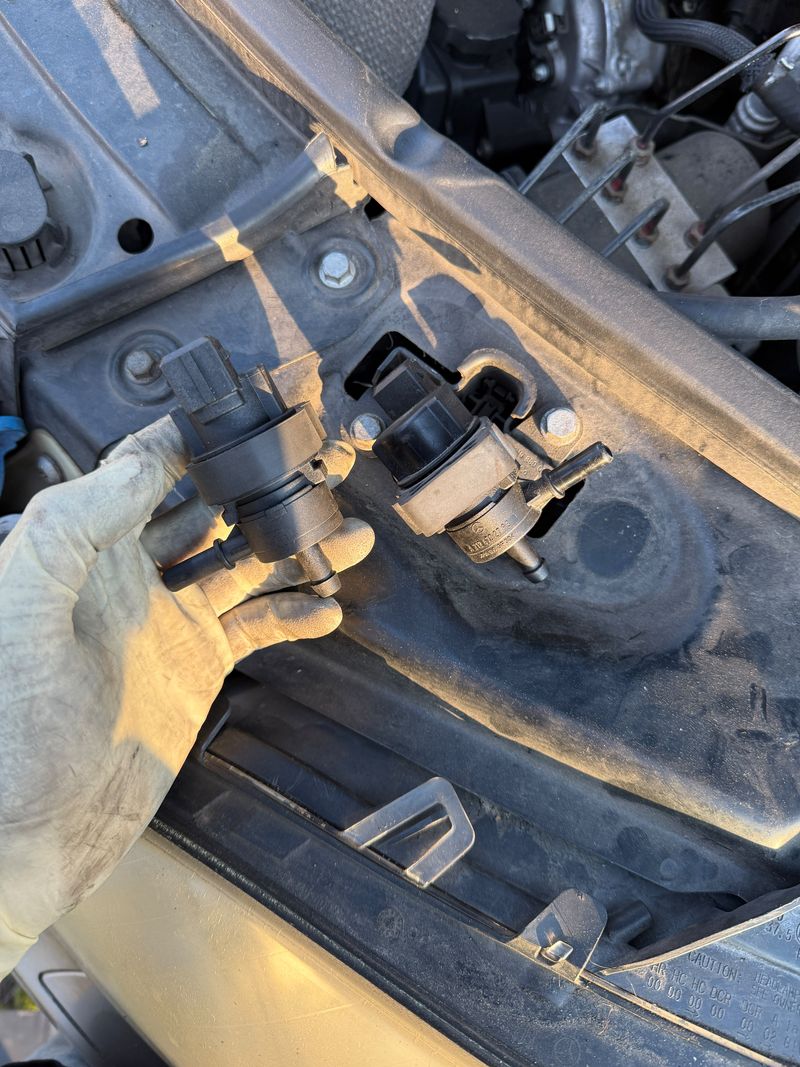 Old Mercedes-Benz EVAP purge valve held next to the new one mounted in the engine bay